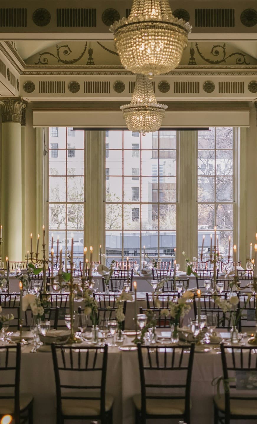 A ballroom under crystal chandeliers, laid for dinner