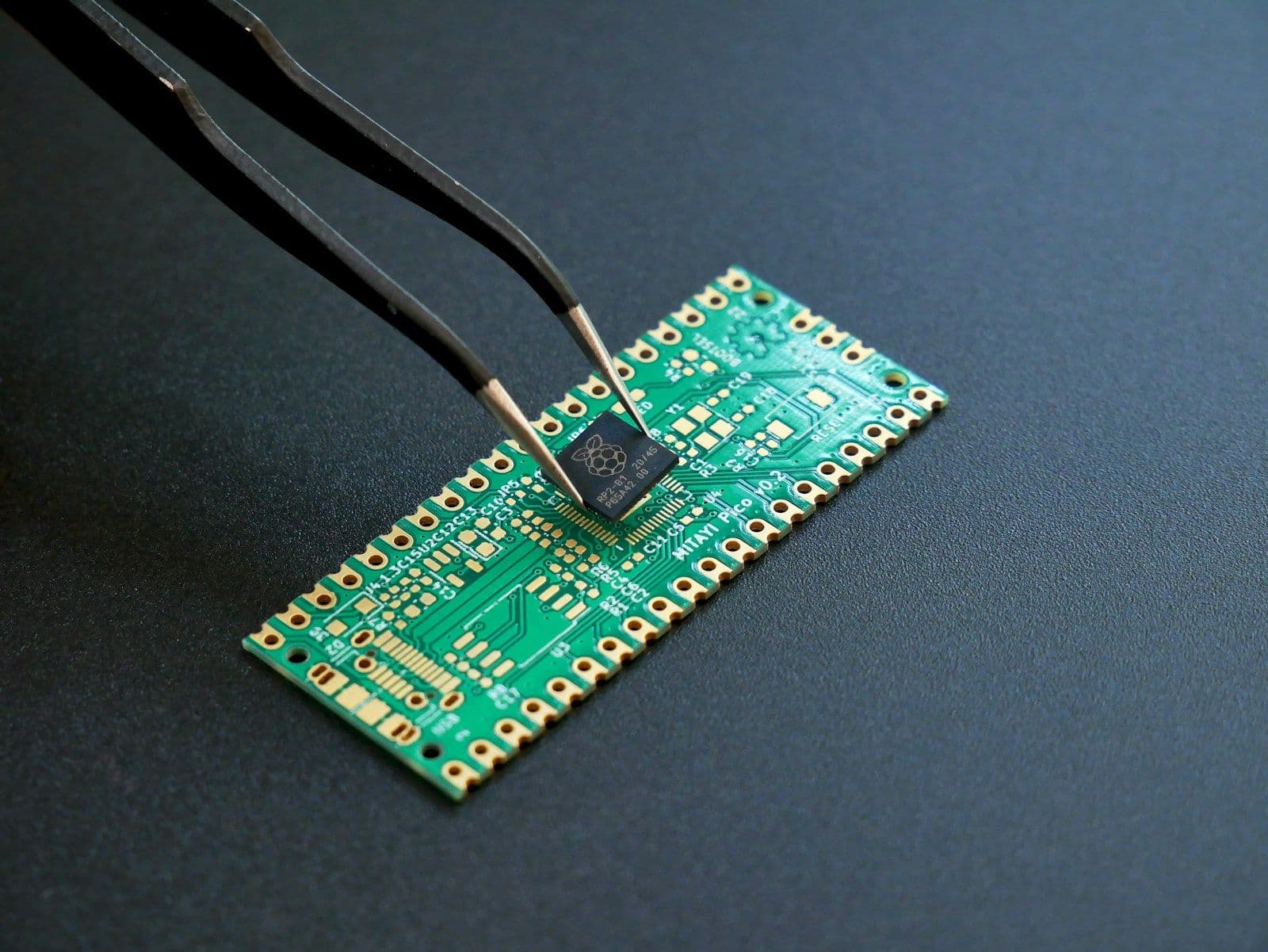A microchip placed on a green circuit board with tweezers