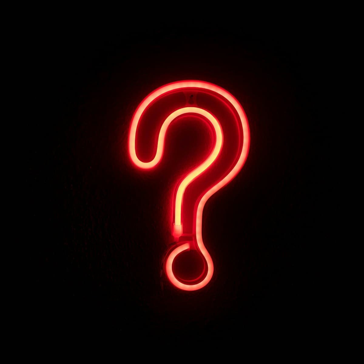 A glowing red neon question mark on a black wall