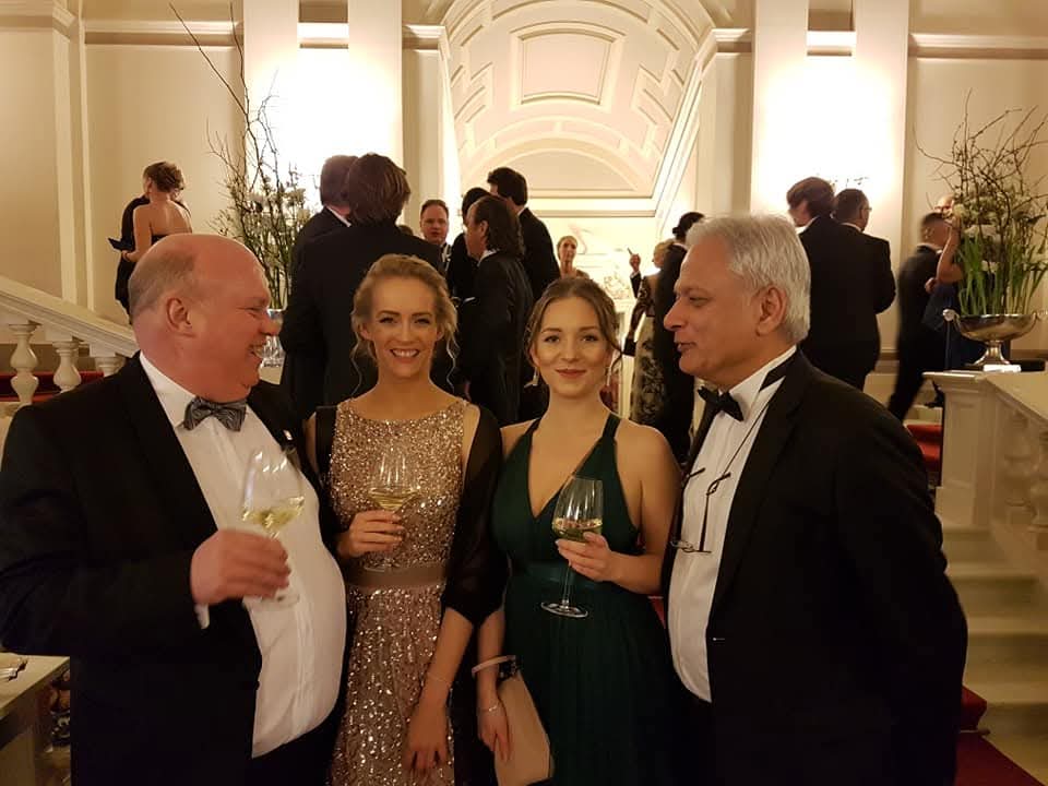 Four guests in black tie raising glasses at an evening reception on a grand staircase