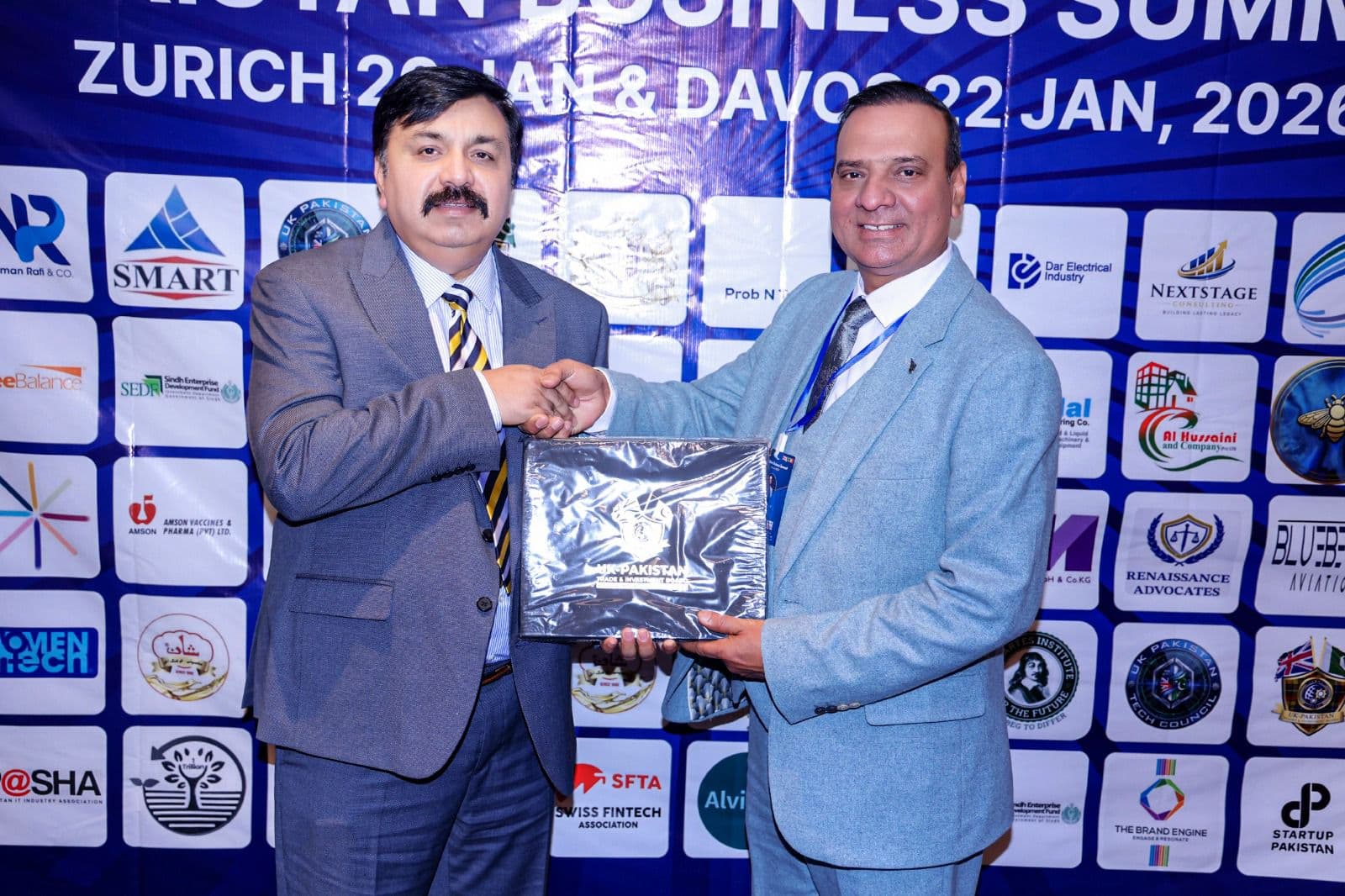 A presentation and handshake in front of the summit partners wall