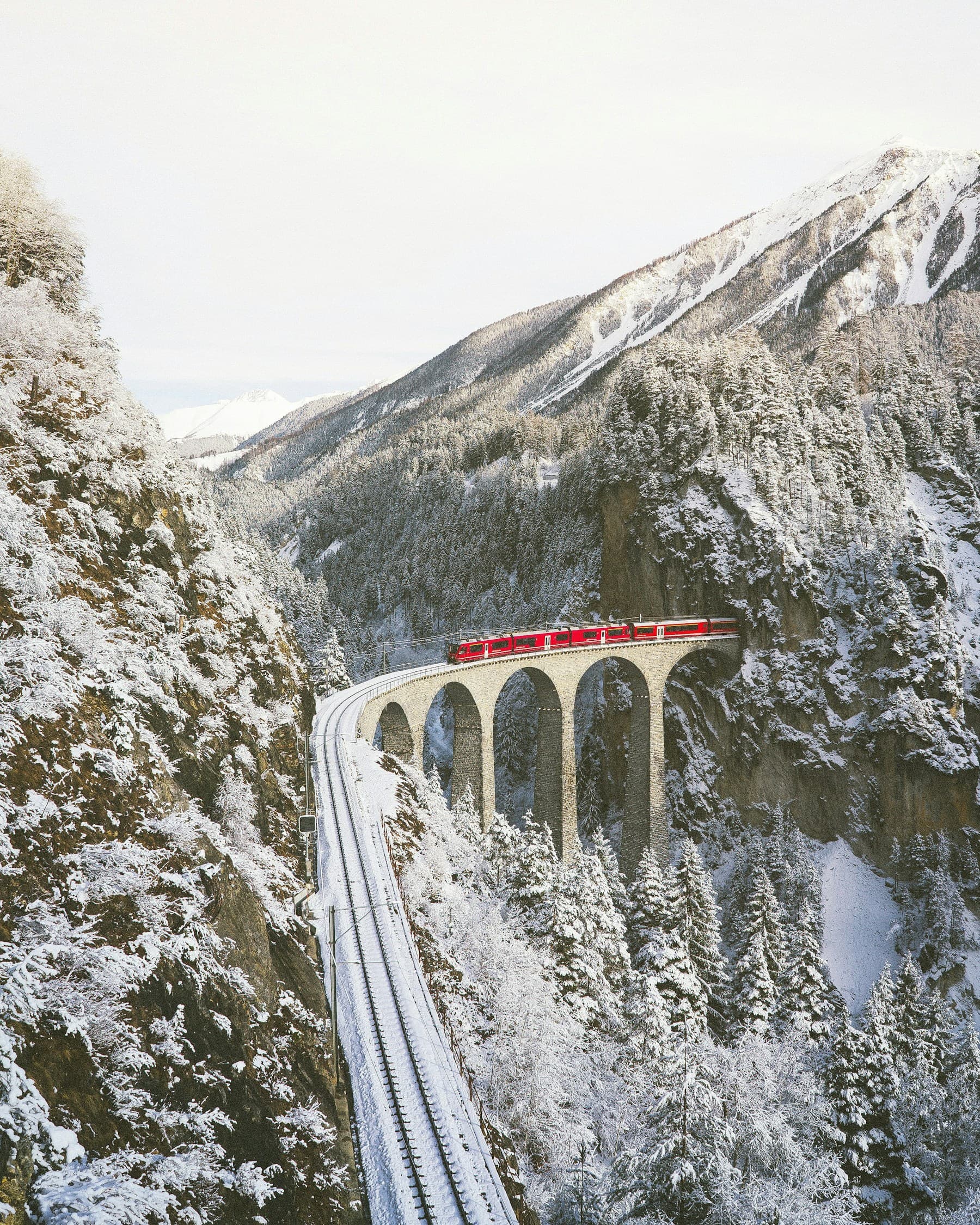 A red Rhaetian Railway train crossing a snowy Alpine viaduct