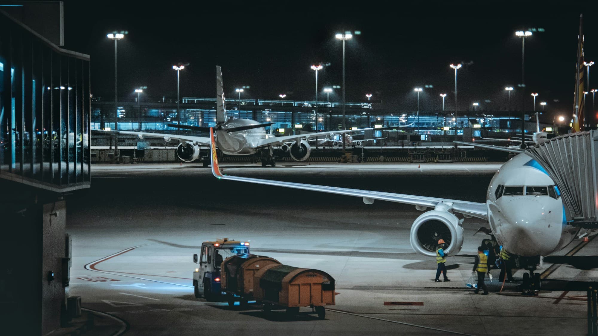 Ground crew and a cargo tug beside an aircraft on an airport apron at night