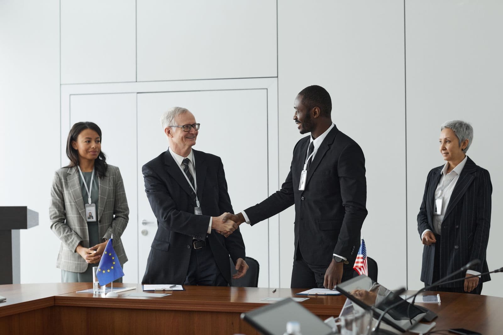 Government and business representatives shaking hands at a delegation meeting, flags on the table